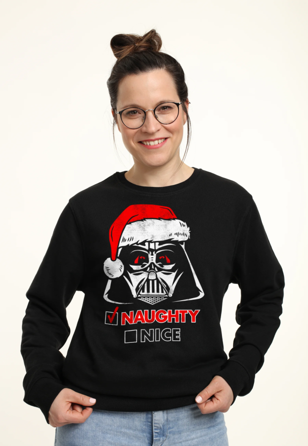 Eine Frau trägt einen „Star Wars“-Weihnachtspullover mit Darth Vader und einer „Naughty“-Markierung.