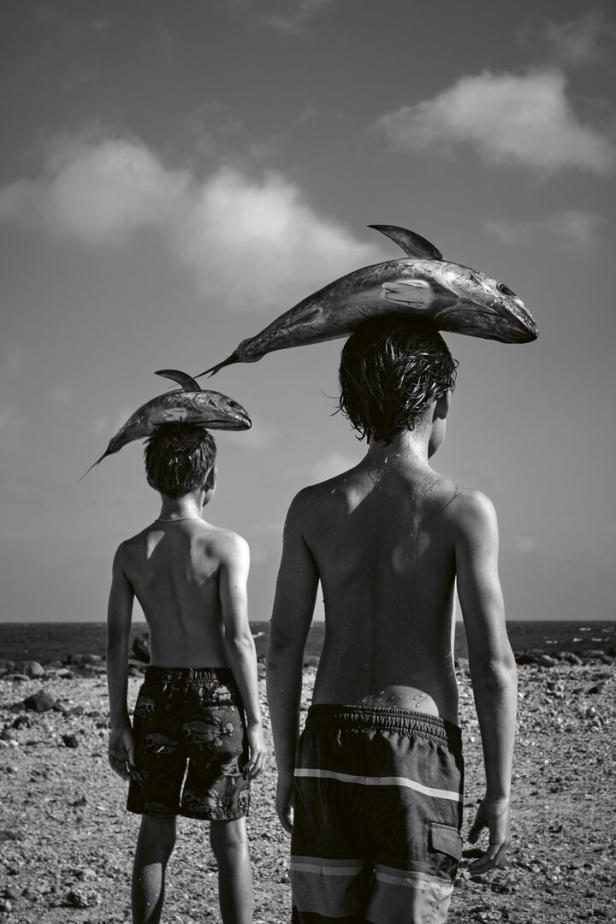 Zwei Jungen balancieren tote Fische auf ihren Köpfen am Strand.