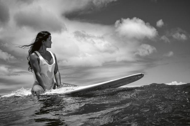Eine Frau mit langen Haaren sitzt auf einem Surfbrett.