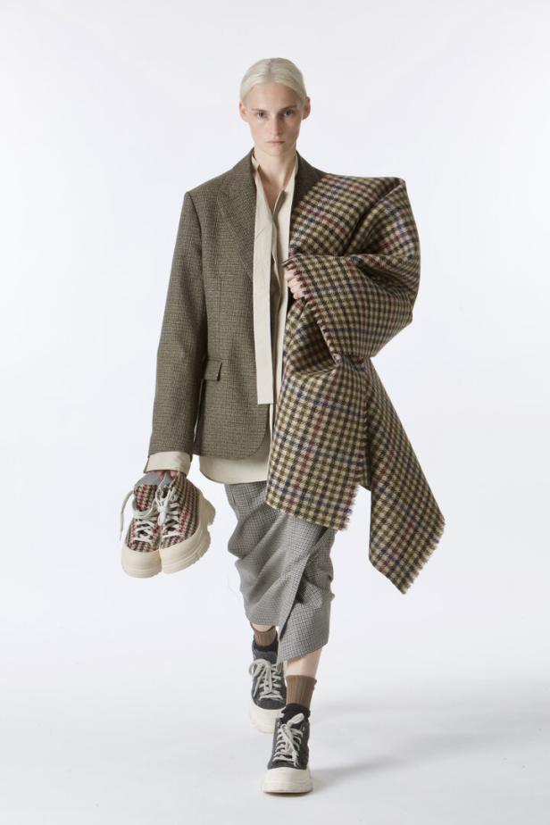 Eine Frau in einem Tweed-Blazer und karierter Hose, die passende Schuhe und einen Schal trägt.