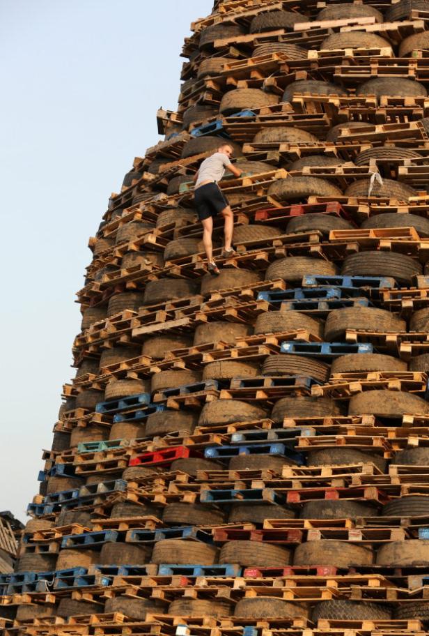 Ein Mann klettert auf einen riesigen Turm aus Paletten und Reifen.