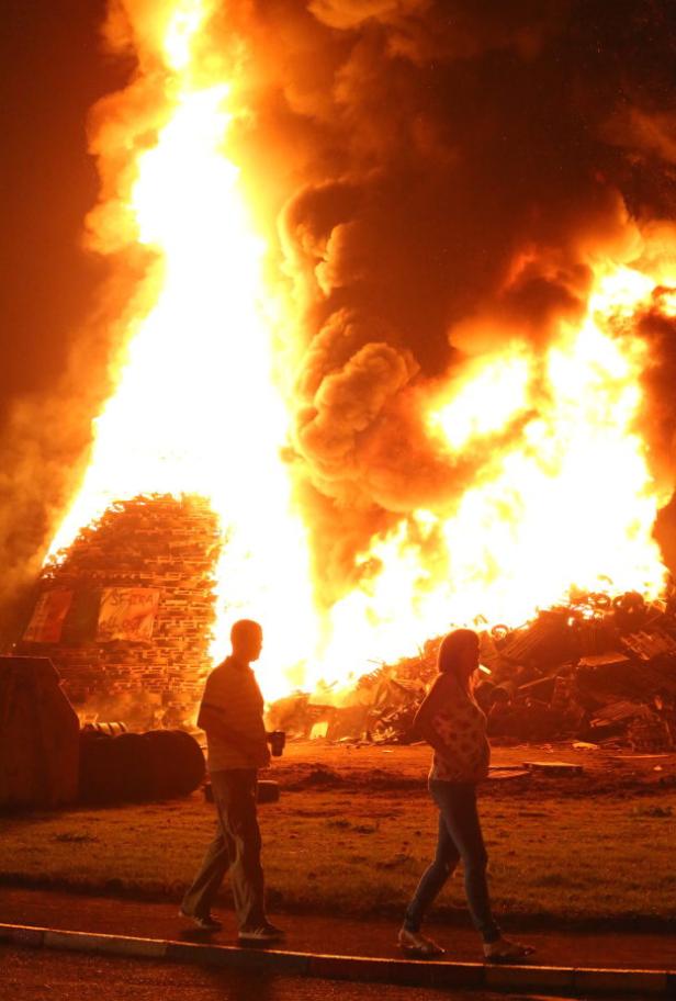 Ein Paar geht an einem riesigen Lagerfeuer vorbei.