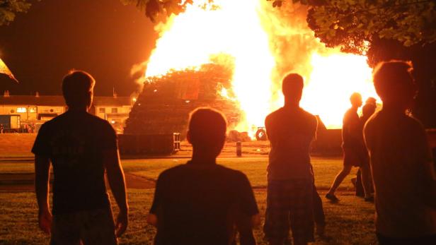 Eine Gruppe von Menschen beobachtet ein großes Lagerfeuer in der Nacht.