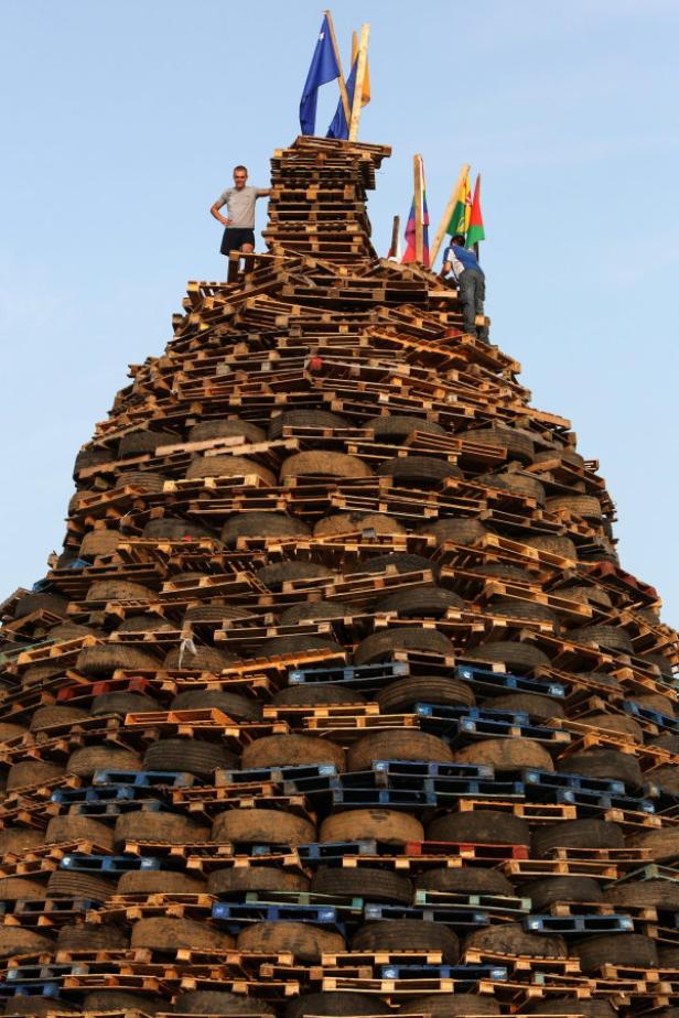 Ein riesiger Turm aus Paletten und Reifen mit zwei Personen und Flaggen auf der Spitze.