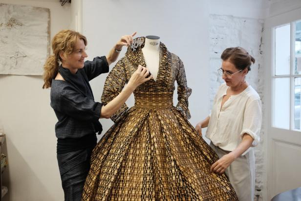 Zwei Frauen arrangieren ein auffälliges, gemustertes Kleid auf einer Schneiderpuppe.