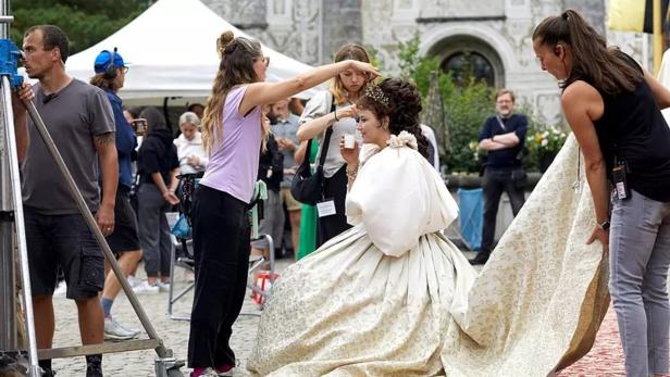 Eine Frau im historischen Kleid wird am Set von Maskenbildnern und Kameraleuten umgeben.