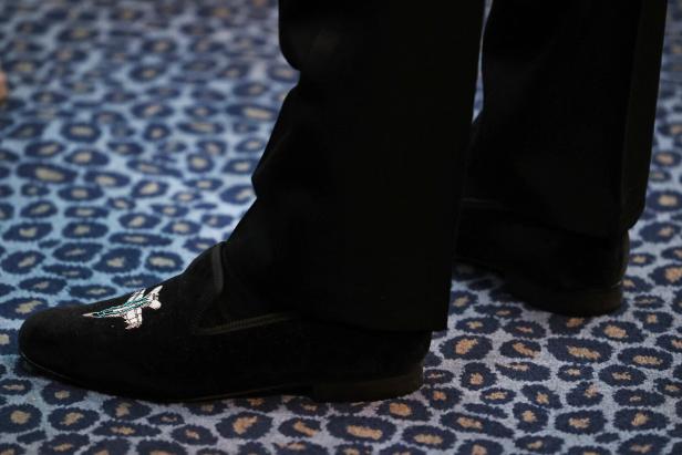Nahaufnahme von Füßen in schwarzen Schuhen mit Flugzeugmuster auf einem Teppich mit Tiermuster.