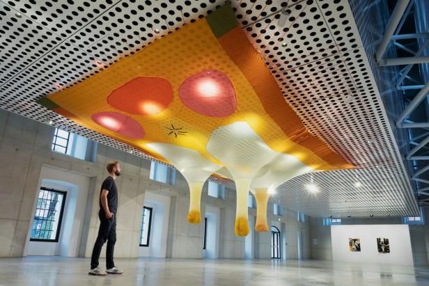 Ein Mann betrachtet eine farbenfrohe, hängende Kunstinstallation in einem Ausstellungsraum.