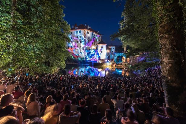 Eine große Menschenmenge sitzt vor einem Schloss, auf das bunte Lichter projiziert werden.