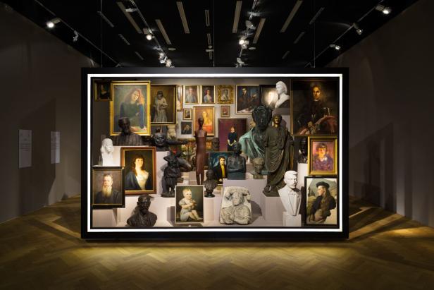Ausstellung mit einer Sammlung von Porträtgemälden und Skulpturen in einem beleuchteten Rahmen.