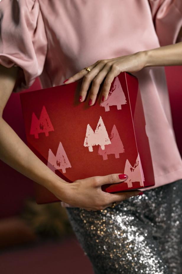 Eine Frau hält eine rote Geschenkbox mit Tannenbaum-Motiv.