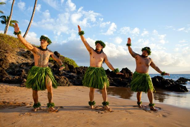 Drei hawaiianische Männer tanzen Hula am Strand.