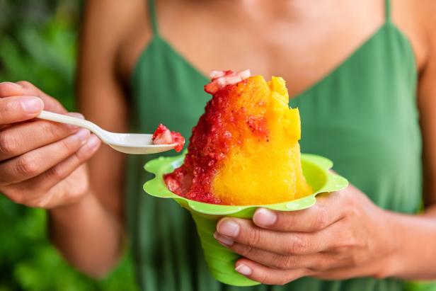 Eine Frau isst ein Schabeis mit Erdbeeren und Mango aus einem grünen Becher.