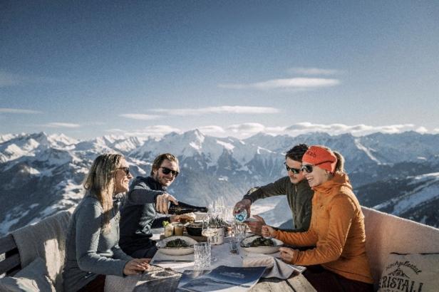 Vier Personen genießen eine Mahlzeit auf einem Berggipfel und erfreuen sich an der atemberaubenden Aussicht. Kulinarik im Zillertal genießen