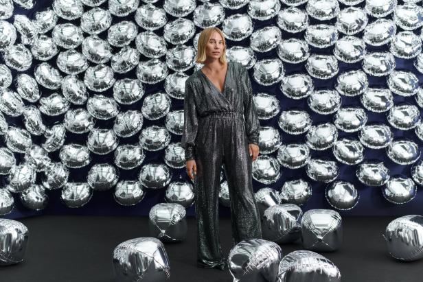 Eine Frau in einem glitzernden Overall steht vor einer Wand aus silbernen Ballons.