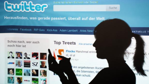 Die Silhouette einer Frau, die ein Smartphone vor einem Twitter-Bildschirm hält.