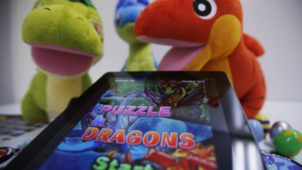 Ein Tablet zeigt das Spiel „Puzzle & Dragons“, umgeben von bunten Plüschtieren.