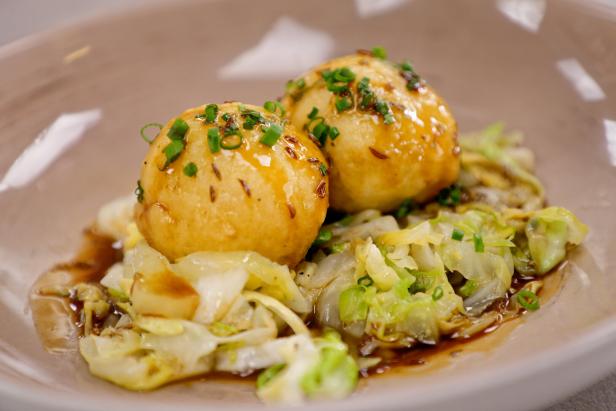 Zwei Kartoffelknödel liegen auf einem Bett aus Krautsalat und sind mit Schnittlauch garniert.