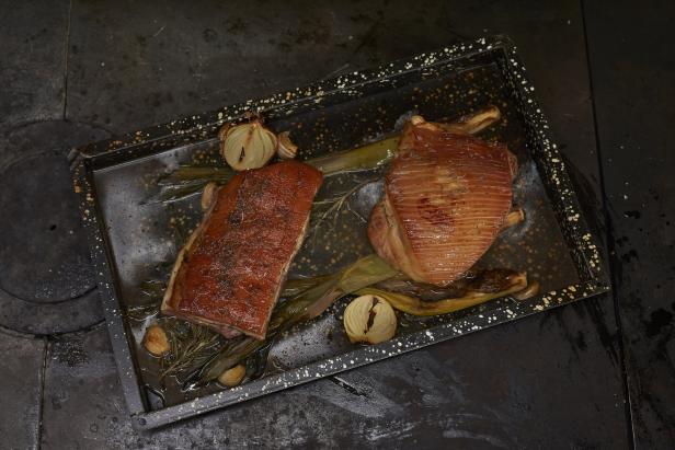 Zwei Stücke gebratenes Fleisch mit Zwiebeln und Kräutern auf einem Backblech.