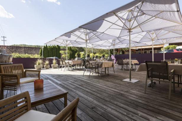 Ein Restaurant mit Tischen und Stühlen auf einer Holzterrasse unter großen Sonnenschirmen.