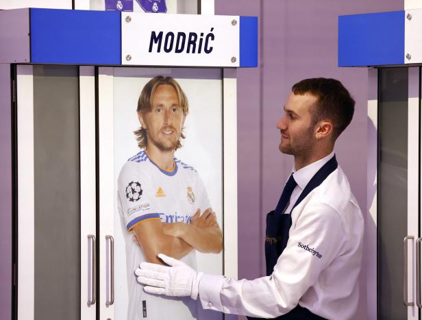 Ein Mann in Sotheby's-Kleidung steht neben einem Porträt von Luka Modrić.