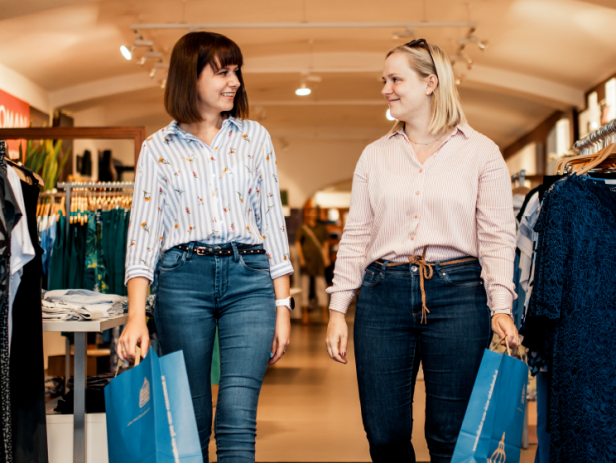 Zwei junge Frauen verlassen mit Einkaufstaschen einen Klamottenladen.