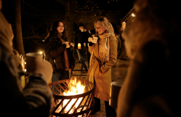 Zwei Frauen stehen um ein offenes Feuer und trinken Glühwein.