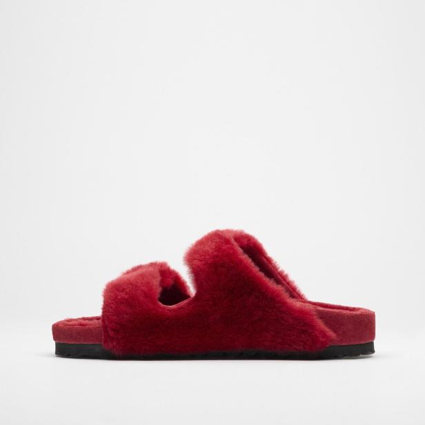 Ein roter, flauschiger Slipper mit zwei Riemen steht auf einem weißen Hintergrund.