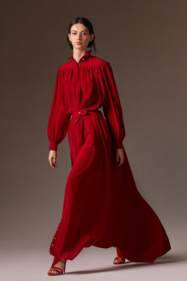 Eine Frau in einem langen, roten Kleid mit Gürtel und passenden Sandalen.