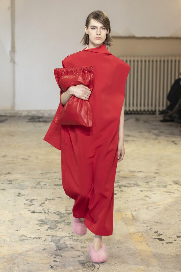 Eine Frau in einem roten Kleid mit passender Tasche und rosa Hausschuhen auf einem Laufsteg.