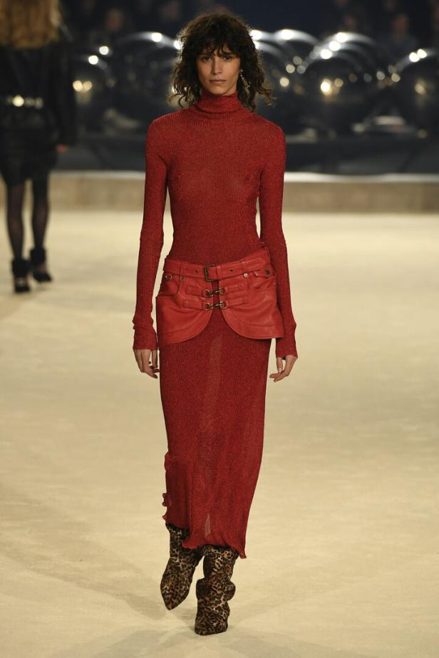 Ein Model auf dem Laufsteg trägt ein rotes Rollkragenkleid mit einem roten Ledergürtel und Stiefeln mit Leopardenmuster.
