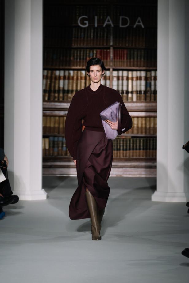 Eine Frau präsentiert ein Outfit von Giada auf dem Laufsteg vor einem Bücherregal.