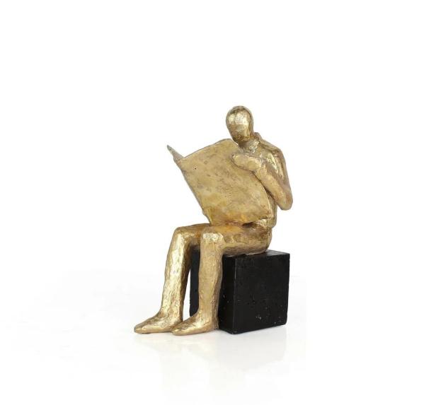 Eine goldene Skulptur einer sitzenden Person, die ein Buch liest.