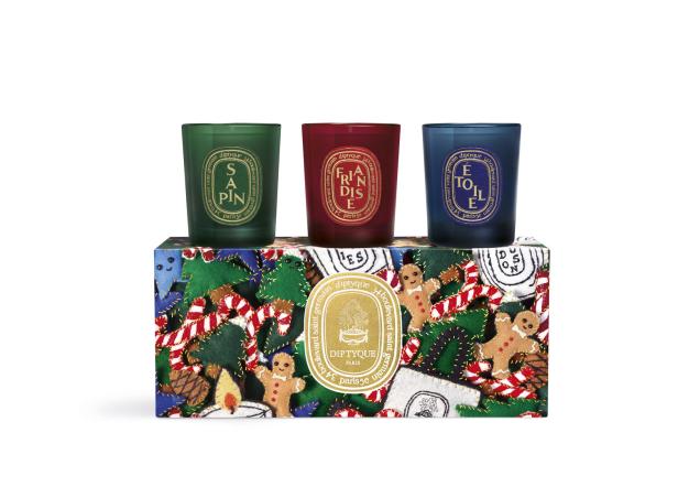 Drei Duftkerzen von Diptyque in Grün, Rot und Blau auf einer weihnachtlich verzierten Schachtel.