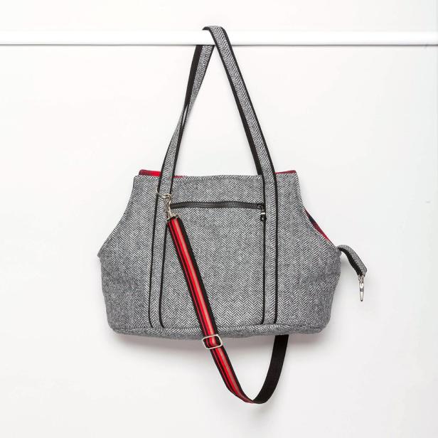 Eine graue Handtasche mit Fischgrätenmuster hängt an einer Stange.