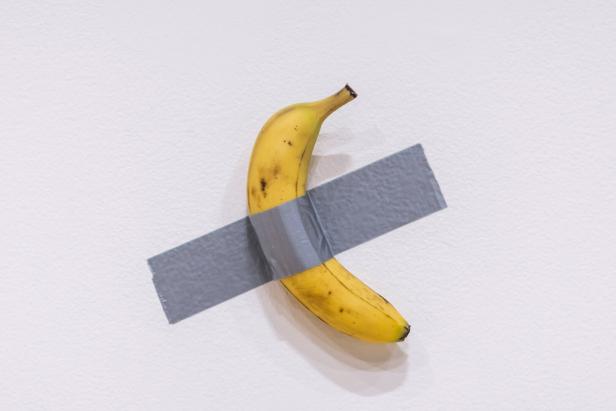 Eine Banane ist mit einem Stück Panzertape an einer weißen Wand befestigt.