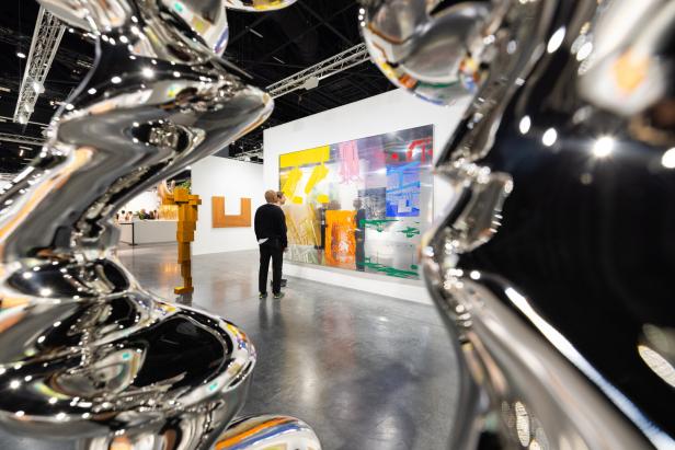 Besucher betrachten Kunstwerke auf einer Kunstausstellung, darunter eine große, farbenfrohe Leinwand und glänzende Skulpturen.