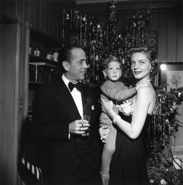 Humphrey Bogart, Lauren Bacall und ihr Kind vor einem Weihnachtsbaum.