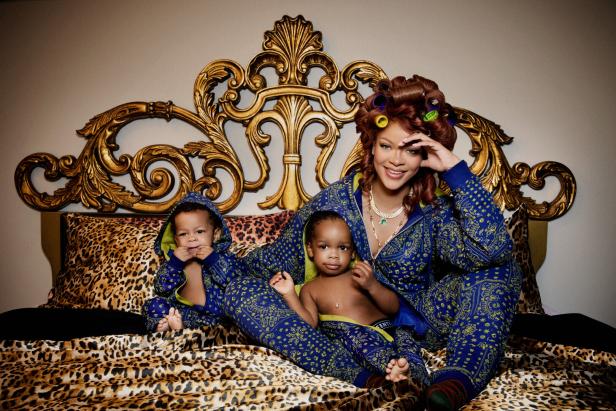 Rihanna sitzt mit Lockenwicklern im Haar und ihren zwei Söhnen auf einem Bett mit Leopardenmuster.