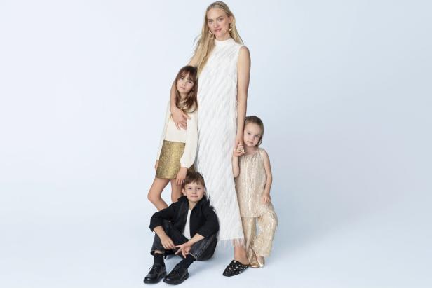 Eine Frau in einem weißen Kleid posiert mit drei Kindern in festlicher Kleidung.