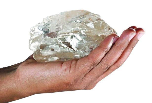 Eine Hand hält einen großen, ungeschliffenen Diamanten.