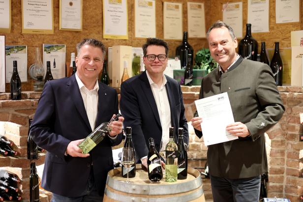 Drei Männer präsentieren Weine des Weinguts Cobenzl auf einem Weinfass.