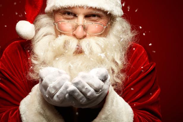 Der Weihnachtsmann mit Brille pustet Schnee in die Kamera.