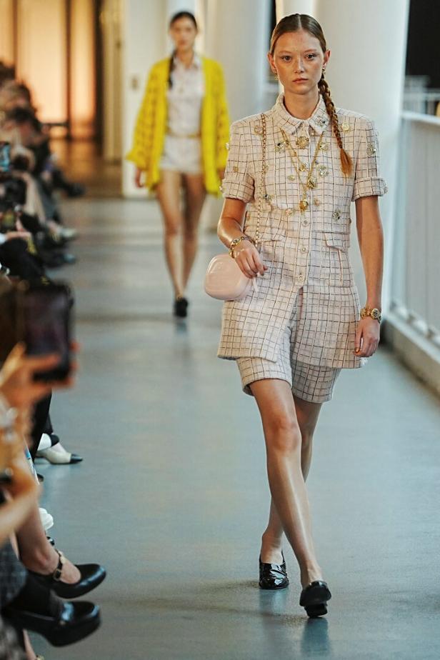 Ein Model präsentiert ein kariertes Chanel-Ensemble mit Shorts auf einem Laufsteg.