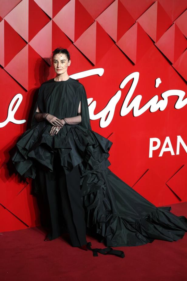Eine Frau in einem schwarzen, extravaganten Kleid mit Schleier posiert vor einem roten Hintergrund.