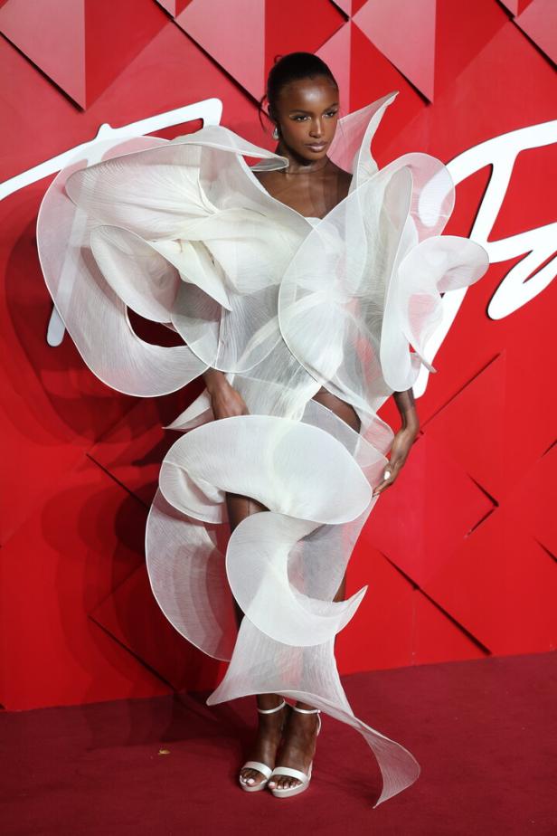 Eine Frau in einem weißen, extravaganten Kleid auf einem roten Teppich.
