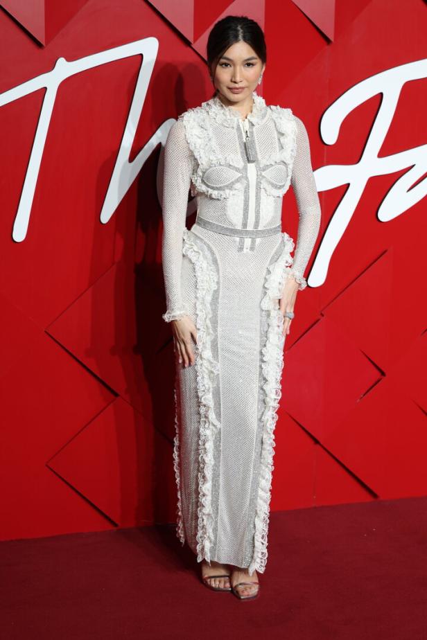 Gemma Chan in einem langen, weißen Kleid mit Rüschen auf einem roten Teppich.