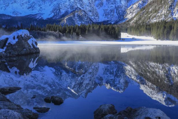 Ein Gebirg spiegelt sich an einem schönen Wintertag im See.