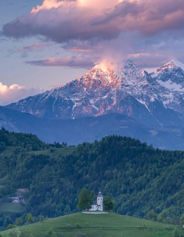 Eine Kirche steht auf einem Hügel - dahinter erhebt sich ein mit Schnee bedeckter Berg.