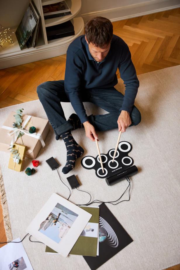 Ein Mann sitzt auf einem Teppich und spielt auf einem elektronischen Schlagzeug.